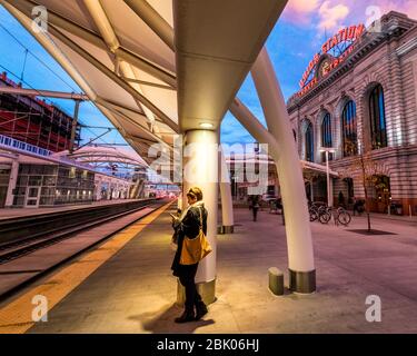 Ein Pendler überprüft ihr Telefon, während er auf einen Stadtzug in Union Station, Denver, Colorado, USA verzichtet. Stockfoto