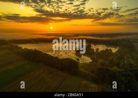 Luftaufnahme eines schönen Sees bei Sonnenaufgang mit nebligen Bäumen umgeben Stockfoto
