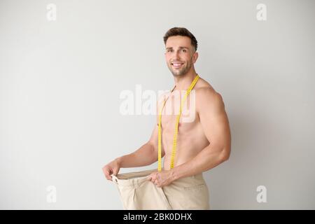 Schöne muskulöse Mann in lockeren Hosen und mit Maßband auf hellen Hintergrund. Gewicht-verlust-Konzept Stockfoto