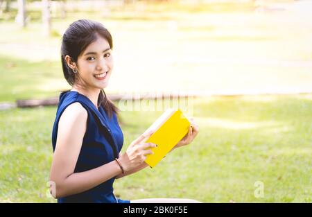 Asiatische Frauen lesen ein gelbes Buch oder Roman, genießen und glücklich, die Frau öffnet ein Buch in der Hand und versehentlich lesen Sie es im Park verschwimmen zurück Stockfoto