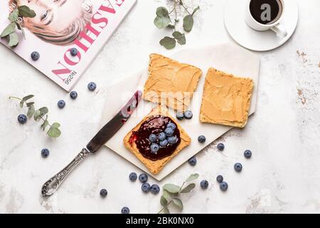 Geröstetes Brot mit Marmelade, Erdnussbutter und Tasse Kaffee auf weißen Tisch Stockfoto