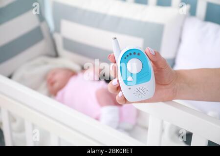 Mutter Holding radio Nanny in der Nähe von Bed mit schlafenden Baby Stockfoto