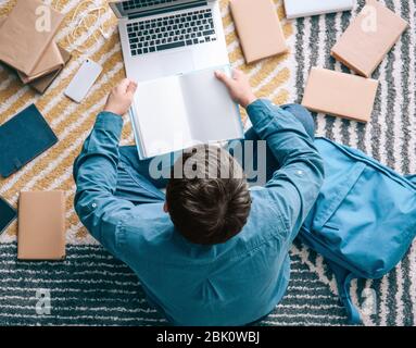 Asiatische Kursteilnehmer mit einer Menge Bücher und Laptop Vorbereitung auf die Prüfung zu Hause Stockfoto