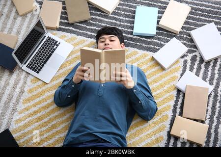 Asiatische Kursteilnehmer mit einer Menge Bücher und Laptop Vorbereitung auf die Prüfung zu Hause Stockfoto