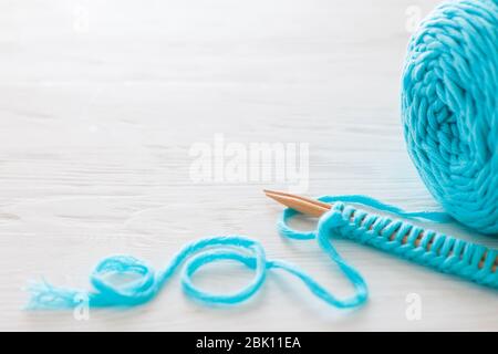 Der Beginn des Strickprozesses. Ein Satz Schlaufen auf Stricknadeln. Weißes Holz. Aquamarinfarbenes Garn. Stockfoto