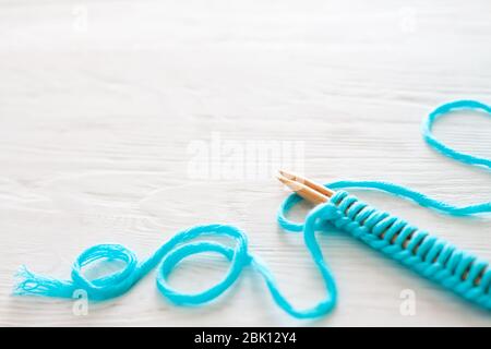 Der Beginn des Strickprozesses. Ein Satz Schlaufen auf Stricknadeln. Weißes Holz. Aquamarinfarbenes Garn. Stockfoto