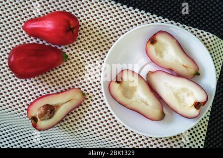 Drei Hälften der Pomarosa-Frucht in einem Teller auf der weißen Oberfläche und mehr Früchte beiseite Stockfoto