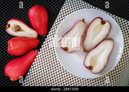 Drei Hälften der Pomarosa-Frucht in einem Teller auf einer weißen Oberfläche und vier weitere Früchte beiseite Stockfoto