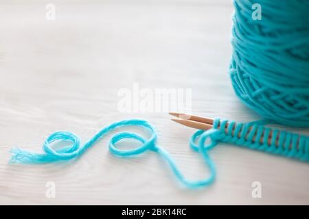 Der Beginn des Strickprozesses. Ein Satz Schlaufen auf Stricknadeln. Weißes Holz. Aquamarinfarbenes Garn. Stockfoto