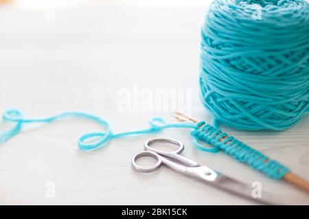 Der Beginn des Strickprozesses. Ein Satz Schlaufen auf Stricknadeln. Weißes Holz. Aquamarinfarbenes Garn. Stockfoto
