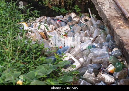 Plastikmüll, der sich an einem Flussufer mit schmutzigem Wasser angesammelt hat Stockfoto