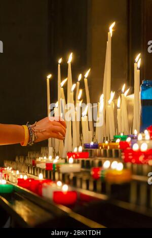 Frau stellt eine Kerze auf Altar in der Kirche.Weibliche Hand legt eine brennende Kerze in der Kirche. Das Konzept des Glaubens an Gott. Stockfoto