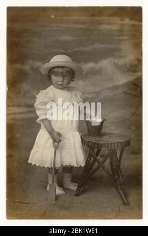 Anfang des 20. Jahrhunderts Seekarte eines kleinen Jungen, der als Mädchen gekleidet war, wie es damals normal war.) mit einem Eimer und Spaten, Eastbourne, Sussex, England, um 1907 Stockfoto