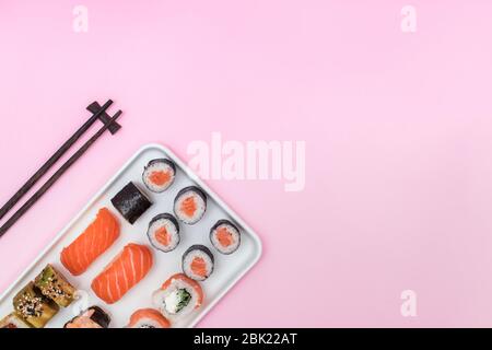 Frisches Sushi und Brötchen und Essstäbchen auf rosa Tisch, Stockfoto