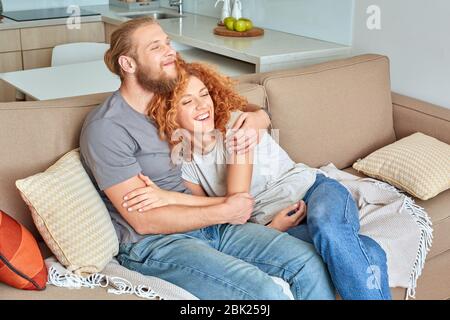 Beziehungskonzept. Ein Paar sitzt auf dem Sofa im Wohnzimmer und lacht fröhlich Stockfoto