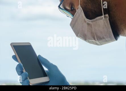 Extreme Nahaufnahme Porträt eines Mannes, der eine chirurgische Maske trägt und auf das Smartphone schaut Stockfoto