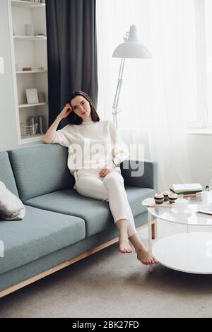 Hübsche junge Frau sitzt auf einem großen Sofa und denkt nach Über etwas Stockfoto