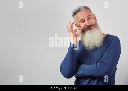 Porträt von reifen grauhaarigen bärtigen Mann in blauen Sweatshirt auf grauem Hintergrund, selektive Fokussierung Stockfoto