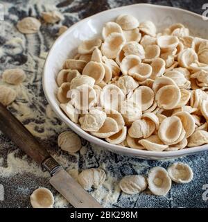 Frische rohe apulische Pasta Orecchiette aus Vollkornmehl auf einem dunklen Tisch aus nächster Nähe Stockfoto