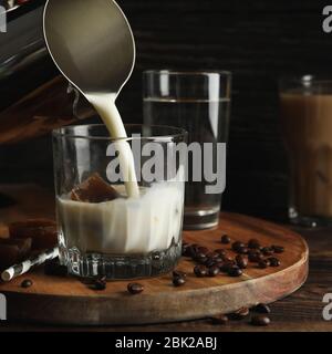 Milch wird in ein Glas Kaffee gegossen. Zusammensetzung mit Eiskaffee Stockfoto