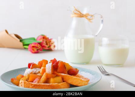 Französischer Toast mit geschmorten Äpfeln und Erdbeeren, mit einer Tasse Kaffee und Tulpenblumen auf einem weißen Holztisch. French Toast oder auch Pain perdu o Stockfoto