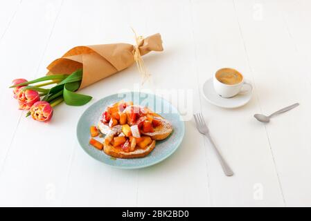 Französischer Toast mit geschmorten Äpfeln und Erdbeeren, mit einer Tasse Kaffee und Tulpenblumen auf einem weißen Holztisch. French Toast oder auch Pain perdu o Stockfoto