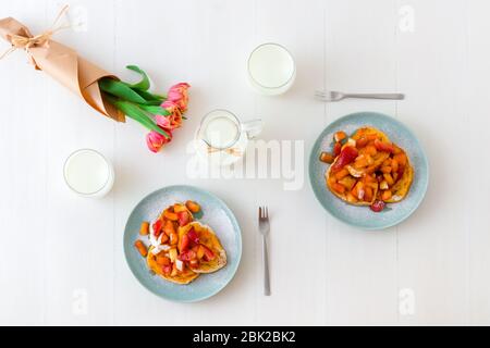 Französischer Toast mit geschmorten Äpfeln und Erdbeeren, mit einer Tasse Kaffee und Tulpenblumen auf einem weißen Holztisch. French Toast oder auch Pain perdu o Stockfoto