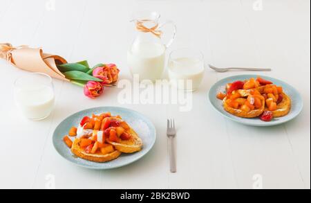 Französischer Toast mit geschmorten Äpfeln und Erdbeeren, mit einer Tasse Kaffee und Tulpenblumen auf einem weißen Holztisch. French Toast oder auch Pain perdu o Stockfoto