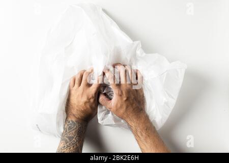 Mann Hand mit Tattoos quetschen eine zerknitterte Schaumplatte isoliert auf weißem Hintergrund. Stockfoto