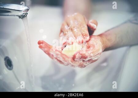 Der Mensch wäscht sich sehr vorsichtig und fleißig die Hände mit Seife über ein weißes Waschbecken, in das Wasser aus dem Wasserhahn fließt. Stockfoto