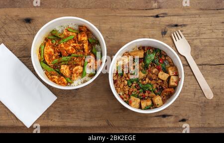 Rühren Sie gebratenes Schweinefleisch und Huhn mit Reis in Papierkartons, zum Mitnehmen asiatische Lebensmittel Lieferung auf Holzhintergrund, Draufsicht Stockfoto