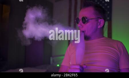 Der amerikanische Hookah Smoker atmet EINE Rauchwolke in Neonlichtern aus Stockfoto