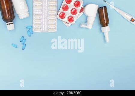 Verschiedene Medikamente, das Thermometer, sprüht aus der verstopften Nase und den Schmerz in der Kehle auf dem blauen Hintergrund. Stockfoto