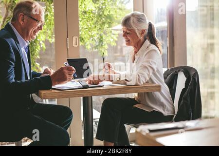 Geschäftspartner in einem Café, die Vertragsdokumente unterzeichnen. Eine Seniorin zeigt, wo man die Zeitung einem Geschäftsmann in einem Café unterschreiben kann. Stockfoto