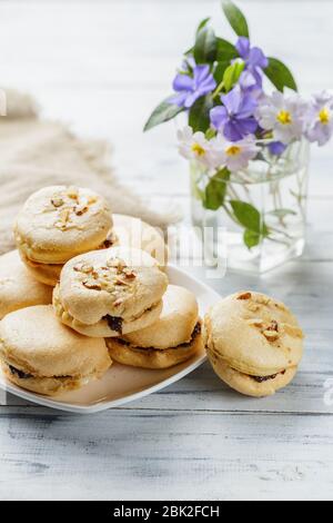 Butterkekse mit Marmelade auf weißem Holzhintergrund mit Blumen auf dem Hintergrund Stockfoto