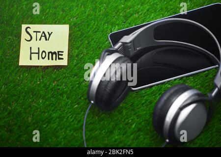 Stay Home Text auf Haftnotizen auf Gras mit Kopfhörern und digitalem Tablet Stockfoto