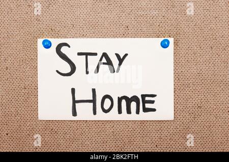 Haftnotiz mit Stay Home Text, der durch Druckstifte an der Pinnwand befestigt ist Stockfoto