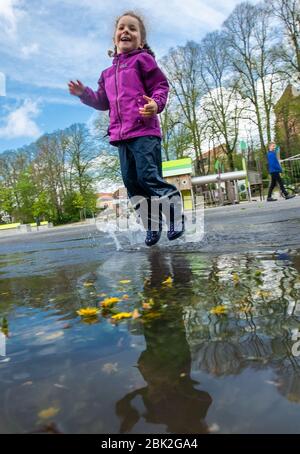 01. Mai 2020, Mecklenburg-Vorpommern, Grevesmühlen: Die vierjährige Isabel springt auf dem Spielplatz auf der Bürgerwiese in eine Pfütze. Pünktlich zum 1. Mai hat die Landesregierung Mecklenburg-Vorpommerns die Spielplätze nach wochenlanger Schließung im Rahmen der Corona-Schutzmaßnahmen wieder eröffnet. Foto: Jens Büttner/dpa-Zentralbild/dpa Stockfoto