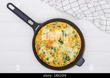 Frittata oder Omelette mit Gemüsemischung in eiserner Pfanne auf weißem Tisch, Draufsicht. Stockfoto