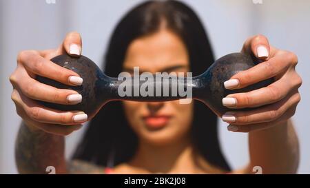 Fit Brünette Frau hält alte Hantel während sonnigen Tag und schaut Sie an Stockfoto