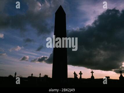 Blick W des runden Turms neben der teilweise zerstörten Kathedrale in Kilmacduagh, Co Galway, Republik Irland: Es ist über 100ft (30m) hoch. Stockfoto