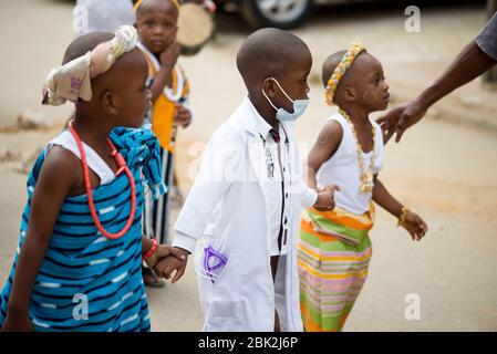 Abidjan, Elfenbeinküste - 13. Februar 2018: Porträt eines nicht identifizierten kleinen Jungen, der als Krankenschwester verkleidet ist, die Hände seiner Freunde hält und in Marsch läuft Stockfoto