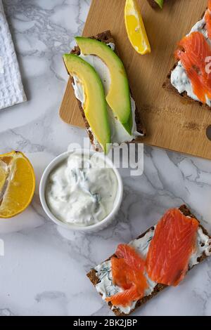 Frühstück am Morgen, zartes hausgemachtes Weichkäse auf Crackern mit geräucherter Forelle und Avocado Stockfoto