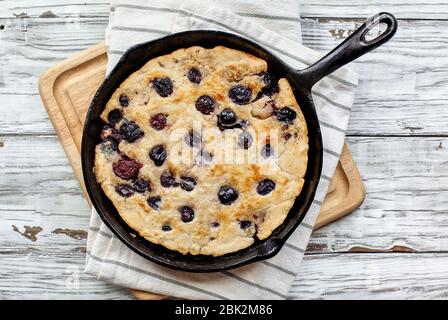 Frisch zubereitetes, hausgemachtes Kirschpflaster, das in einer gusseisernen Pfanne auf einem rustikalen Tisch aus weißem Holz gebacken wird. Bild von oben aufgenommen. Stockfoto