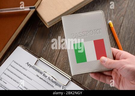 Hand mit einem italienischen Pass, ein Antragsformular im Hintergrund Stockfoto