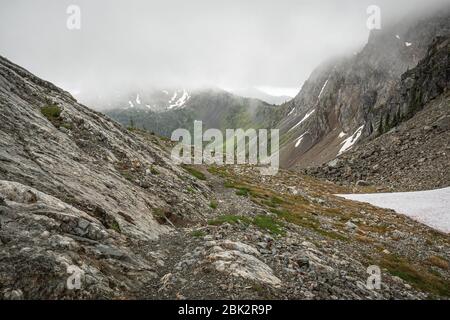 Der Washington Abschnitt des Pacific Crest Trail in den North Cascades mit Blick auf wolkenbedeckte Felsberge und Schnee. Stockfoto