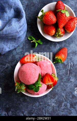 Erdbeer-Eisschaufel mit frischen Erdbeeren in der Schüssel über blauem Steingrund. Leckeres kaltes Sommerdessert. Draufsicht, flacher Lay Stockfoto