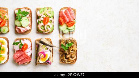 Verschiedene Sandwiches mit Fleisch, Gemüse und Meeresfrüchten. Auswahl offener Sandwiches auf hellem Steingrund mit freiem Textbereich. Leckere gesunde e Stockfoto