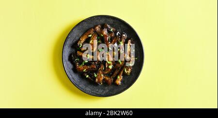 Gebratene Aubergine im koreanischen Stil. Braten Bulgogi Aubergine auf Platte über gelbem Hintergrund mit freiem Textraum. Draufsicht, flaches Lay Stockfoto