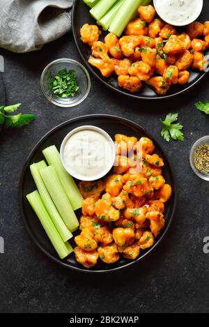 Büffelflügel aus Blumenkohl mit Sellerie und Sauce auf Platte über schwarzem Steingrund. Gesundes Essen, pflanzliches Lebensmittelkonzept. Draufsicht, flacher Lay Stockfoto